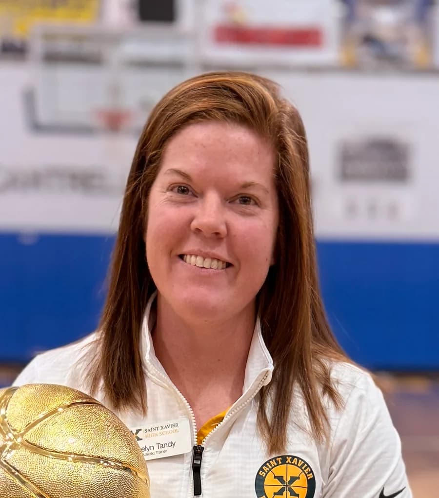 Evelyn Tandy, athletic trainer, in a Saint Xavier High School jacket holding a gold basketball